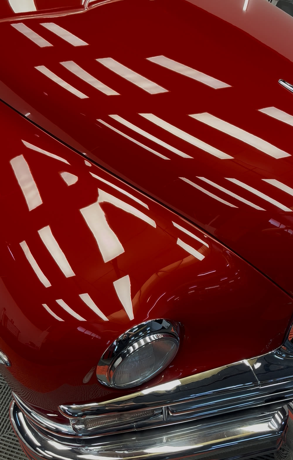 Capó rojo de un Packard clásico recién pulido, con los focos reflejados como en un espejo