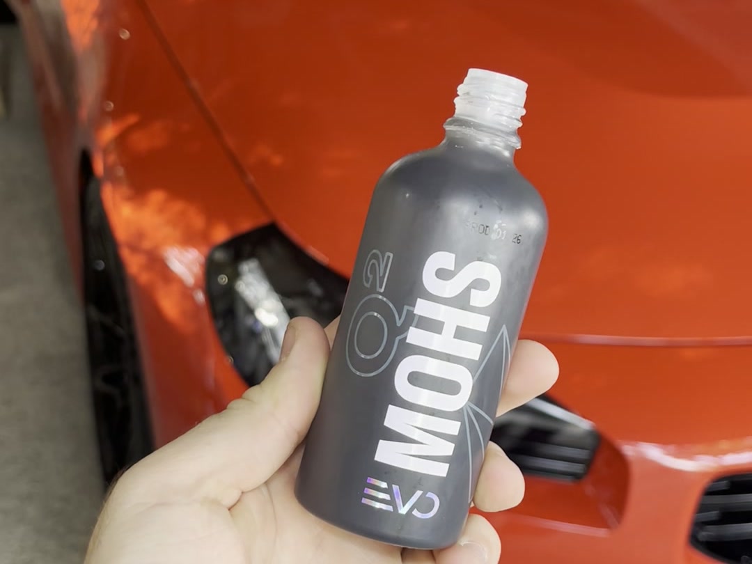 Bote de cerámico GYEON Q² Mohs EVO en la mano, delante de un BMW M2