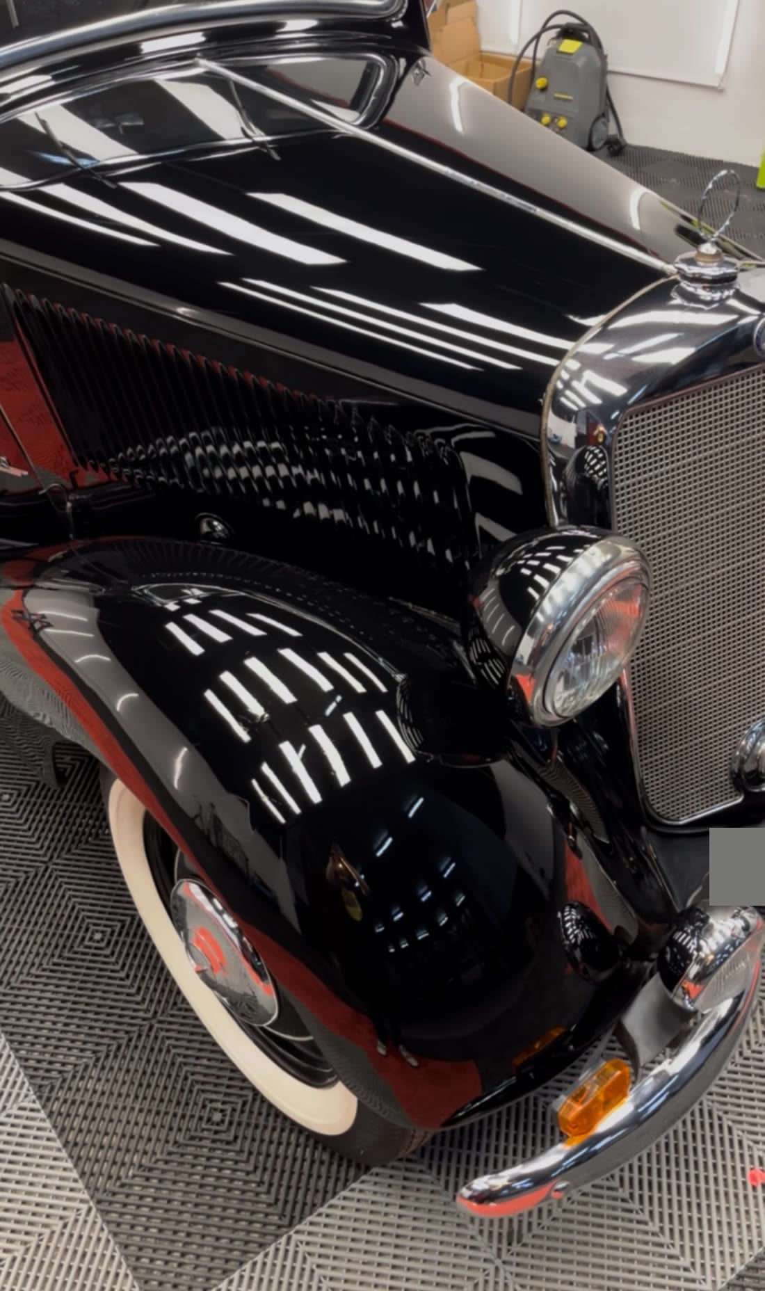 Mercedes clásico negro con la pintura pulida, reflejando las luces como un espejo