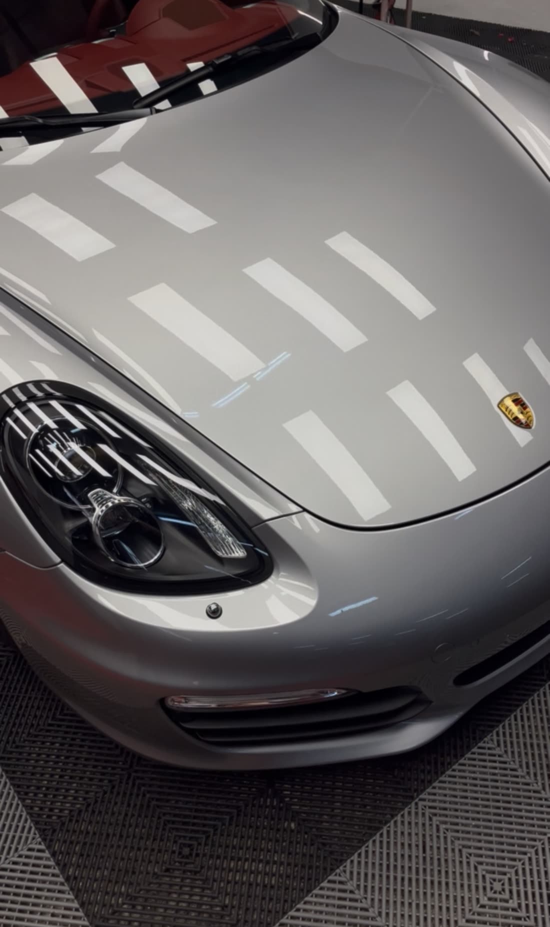Porsche plateado recién pulido, con las luces reflejadas en el capó como en un espejo