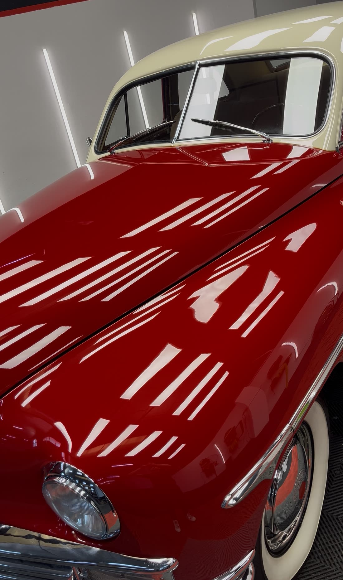 Packard clásico rojo y crema con la pintura pulida, reflejando los focos como un espejo